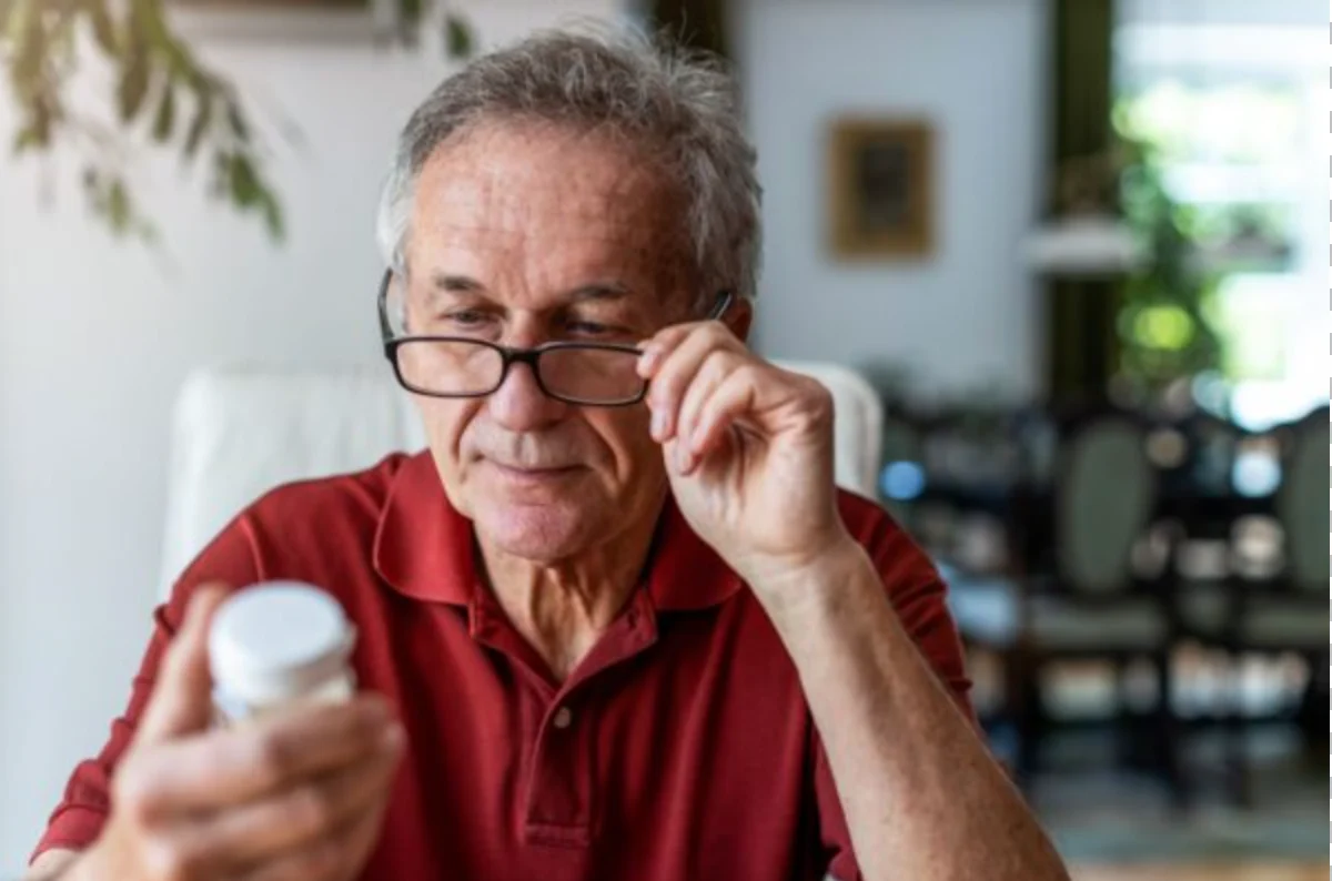 older man pulling his glasses down to read the prescription medication bottle